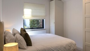 Ein Schlafzimmer mit Bett, Kissen, einem Fenster mit Jalousien, einem Heizkörper und einem Kleiderschrank.