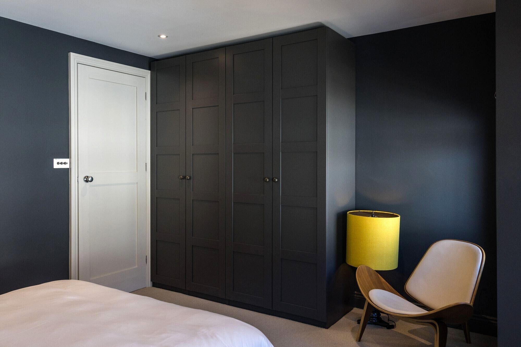 Une chambre à coucher avec un lit, une armoire, une chaise et une lampe.