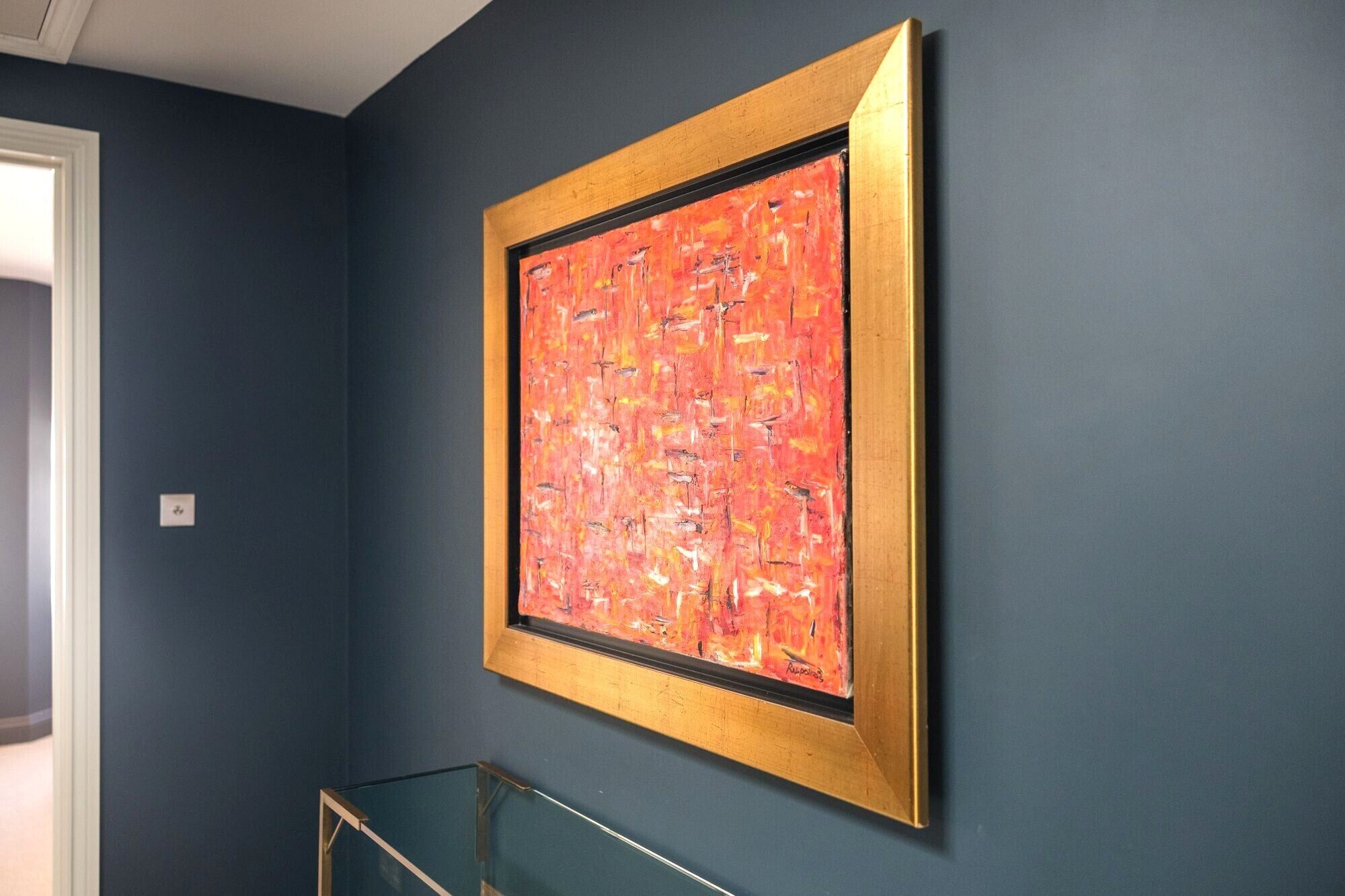 A framed abstract painting on a dark blue wall.