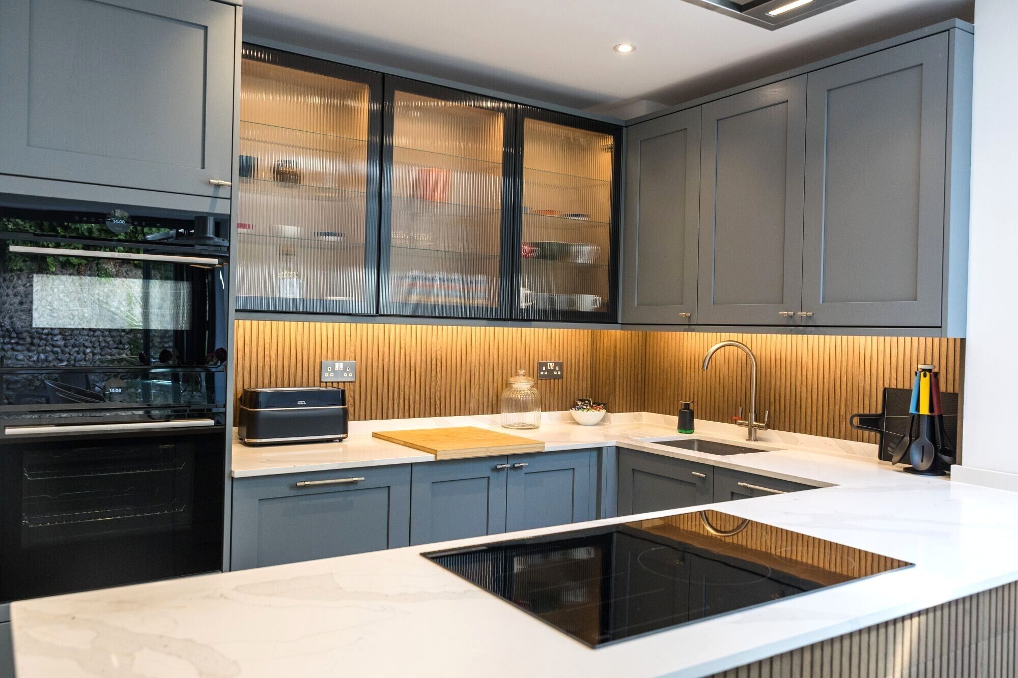 A modern kitchen with grey cabinets, a built-in oven, a microwave, and a large island with a sink.