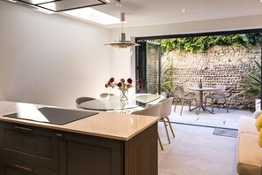 A modern kitchen with a glass island, a dining area with a table and chairs, and a view of a stone wall and greenery outside. - Little Chelsea Escape - stylish & central oasis (Eastbourne)