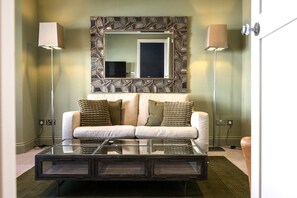 A modern living room with a glass coffee table, a sofa with cushions, a decorative wall mirror, and two floor lamps. - Little Chelsea Escape - stylish & central oasis (Eastbourne)