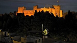 A castle-like structure with multiple towers and a flag, surrounded by trees and buildings. - SEAL of Knight - Castle View - Downtown near the Beach (Rodos)