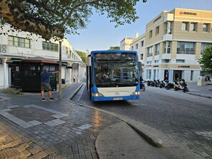 Um ônibus azul em uma rua da cidade, com prédios e motocicletas estacionadas.