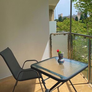Ein Balkon mit Glastisch, einem Stuhl und einer dekorativen Vase mit einer Rose.