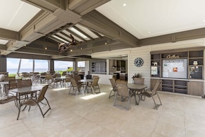 Un grand espace extérieur aménagé pour les repas, avec plusieurs tables et chaises, un coin cuisine et un tableau d’affichage fixé au mur.
