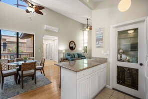 A spacious kitchen with a large island, a dining area with chairs, a ceiling fan, and a view of the outside. - Wailea Ekahi 52D - Wailea 1BR Condo, Garden Lanai, AC, Island Luxury Beach Condo (Kihei)