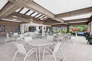 A spacious outdoor area with multiple seating arrangements, including round tables and chairs, and a kitchen area in the background. - Wailea Ekahi 52D - Wailea 1BR Condo, Garden Lanai, AC, Island Luxury Beach Condo (Kihei)