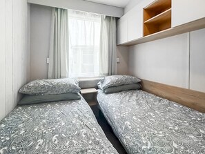 Ein Schlafzimmer mit zwei Betten, einem Fenster mit Vorhängen und einem Holzregal darüber.