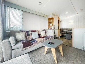 Ein modernes Wohnzimmer mit einer Couch, einem Couchtisch und einer Küchenzeile im Hintergrund.