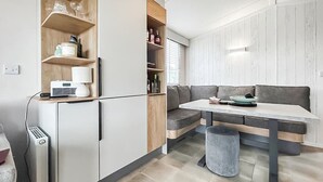 Una cucina compatta con elettrodomestici integrati, un angolo relax con una panca e un piccolo cestino.