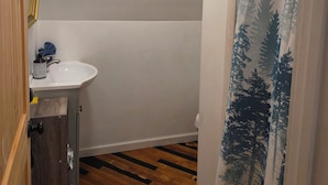 A bathroom with a wooden floor, a white sink, and a shower curtain with a forest pattern. - Charming Loft near Cleveland, TN to relax and rewind in. (Cleveland)
