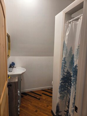 Ein Badezimmer mit Holzboden, einem weißen Waschbecken und einer Duschvorhang mit Waldmuster.