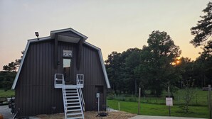 A wooden barn with a ladder leading to a loft entrance, surrounded by a grassy area and trees. - Charming Loft near Cleveland, TN to relax and rewind in. (Cleveland)