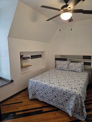 Ein Schlafzimmer mit einem Bett, einem Deckenventilator, einem Bücherregal und einer Wandleuchte.