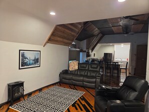 Ein Wohnzimmer mit schwarzem Ledersofa, einem schwarzen Lederstuhl, einem gemusterten Teppich und einem gerahmten Bild an der Wand.