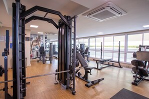 Ein Fitnessraum mit unterschiedlichen Trainingsgeräten, großen Fenstern und Holzboden.
