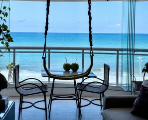 A balcony with a view of the ocean, two chairs, a table with two green apples, and a hanging chair. - Incredible Ocean View•Swimming pools•Academy•Wi-Fi•Vacancy (Salvador)