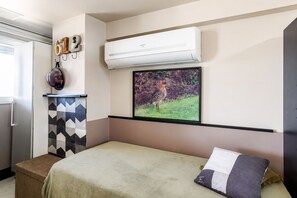 Ein Schlafzimmer mit einem Bett, einer Wandklimaanlage, einem gerahmten Bild eines Vogels und einem Schrank mit geometrischem Muster.