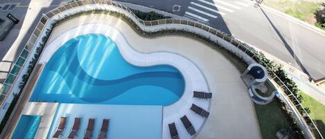 A swimming pool with a wavy edge, surrounded by a low wall and a circular seating area with lounge chairs.