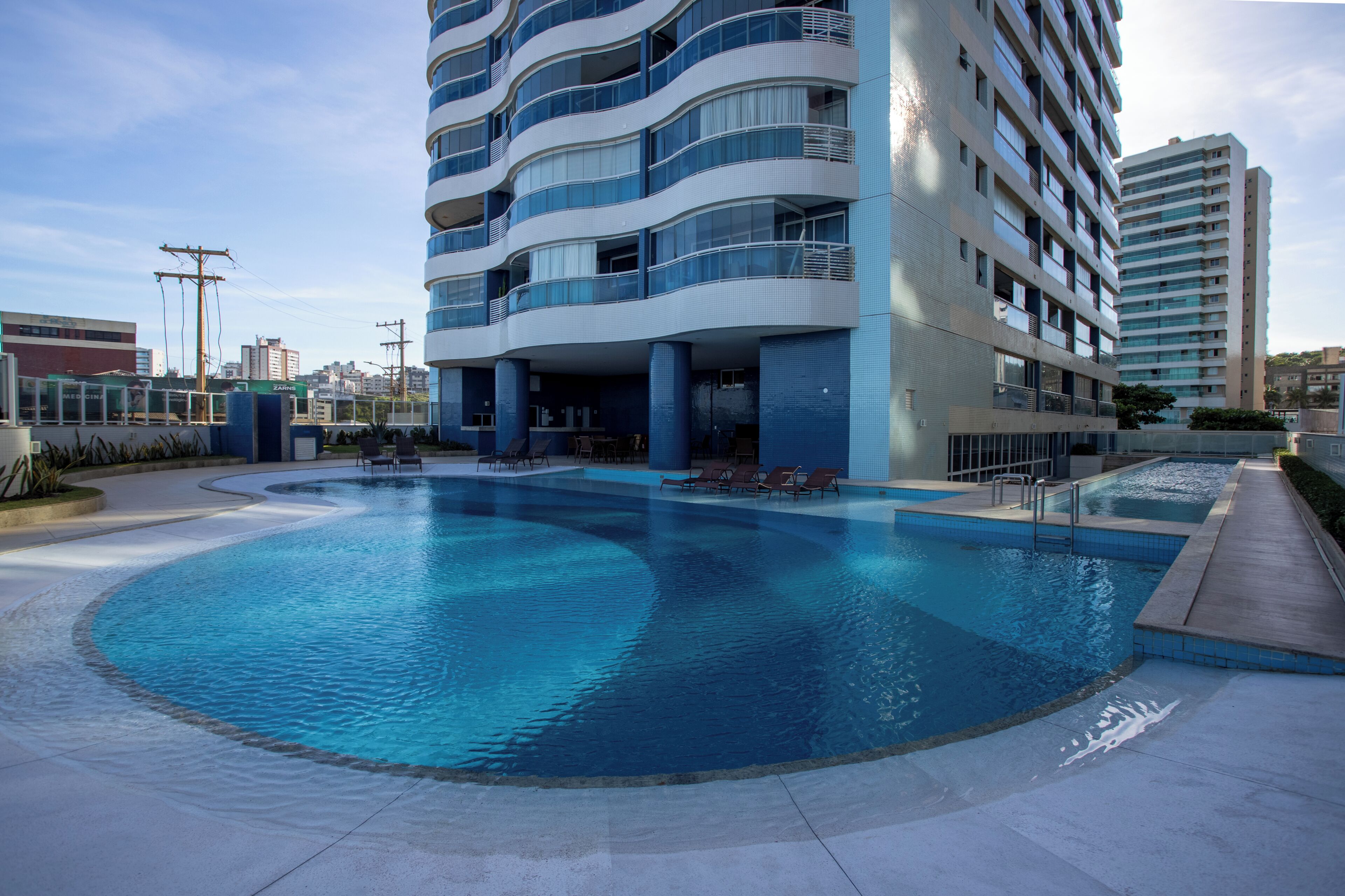 Un edificio moderno con area piscina, che include una grande piscina e lettini.