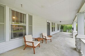 A covered porch with two wooden chairs and a concrete floor.