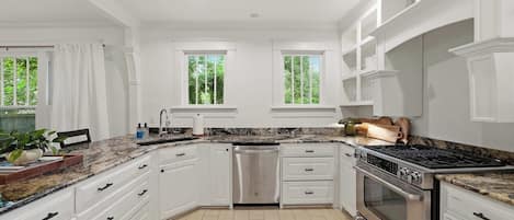 Una cocina moderna con armarios blancos, encimera de granito y campana extractora de acero inoxidable.