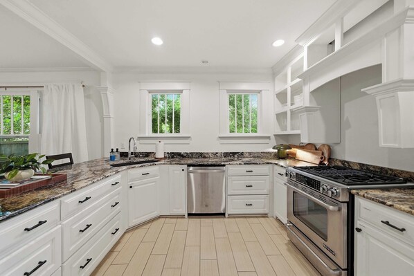 A modern kitchen with white cabinetry, a granite countertop, and a stainless steel range hood.