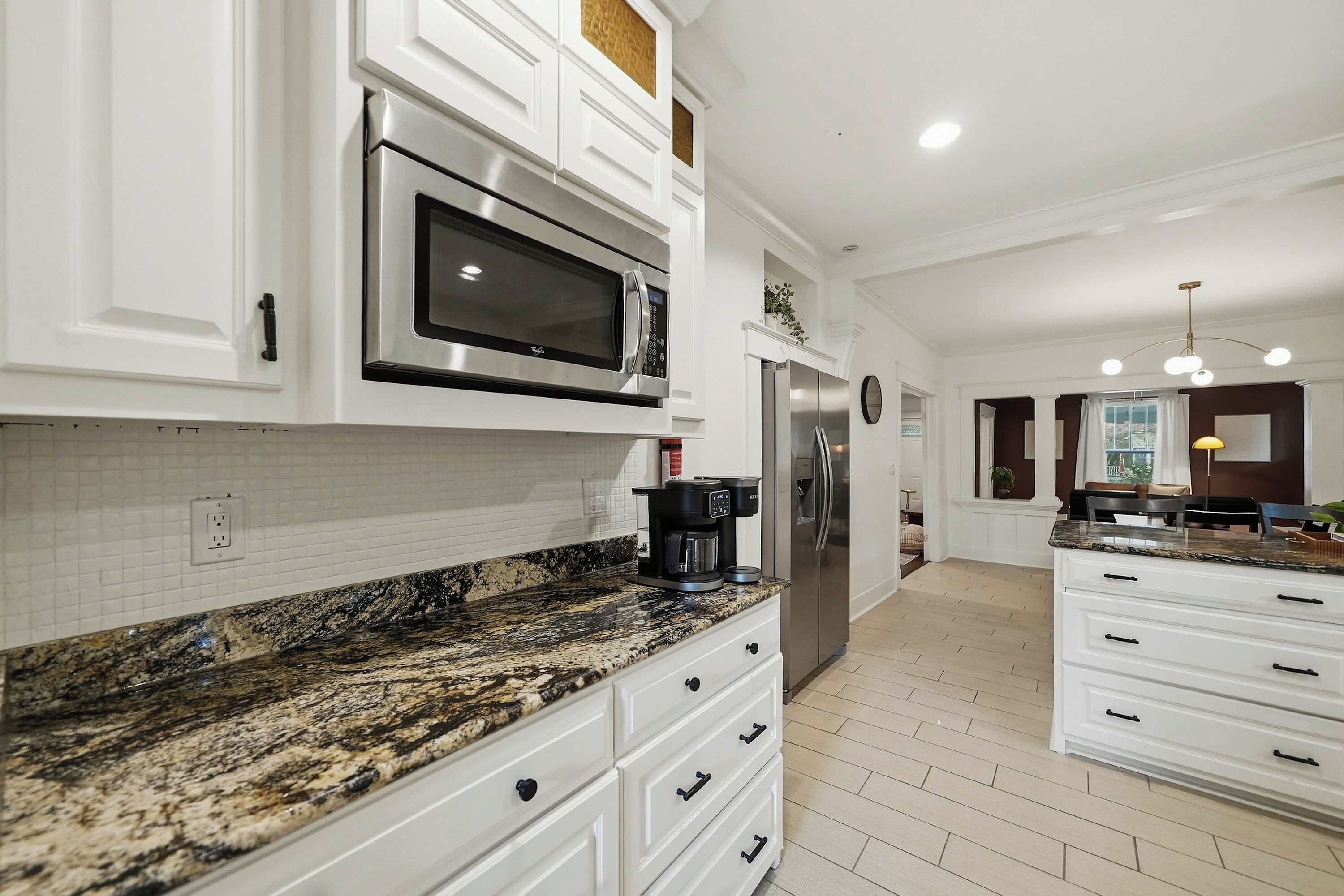 A modern kitchen with white cabinetry, a granite countertop, a built-in microwave, a stainless steel refrigerator, and a coffee maker.