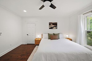 Un dormitorio con cama, mesitas de noche, ventilador de techo, una puerta y una ventana.