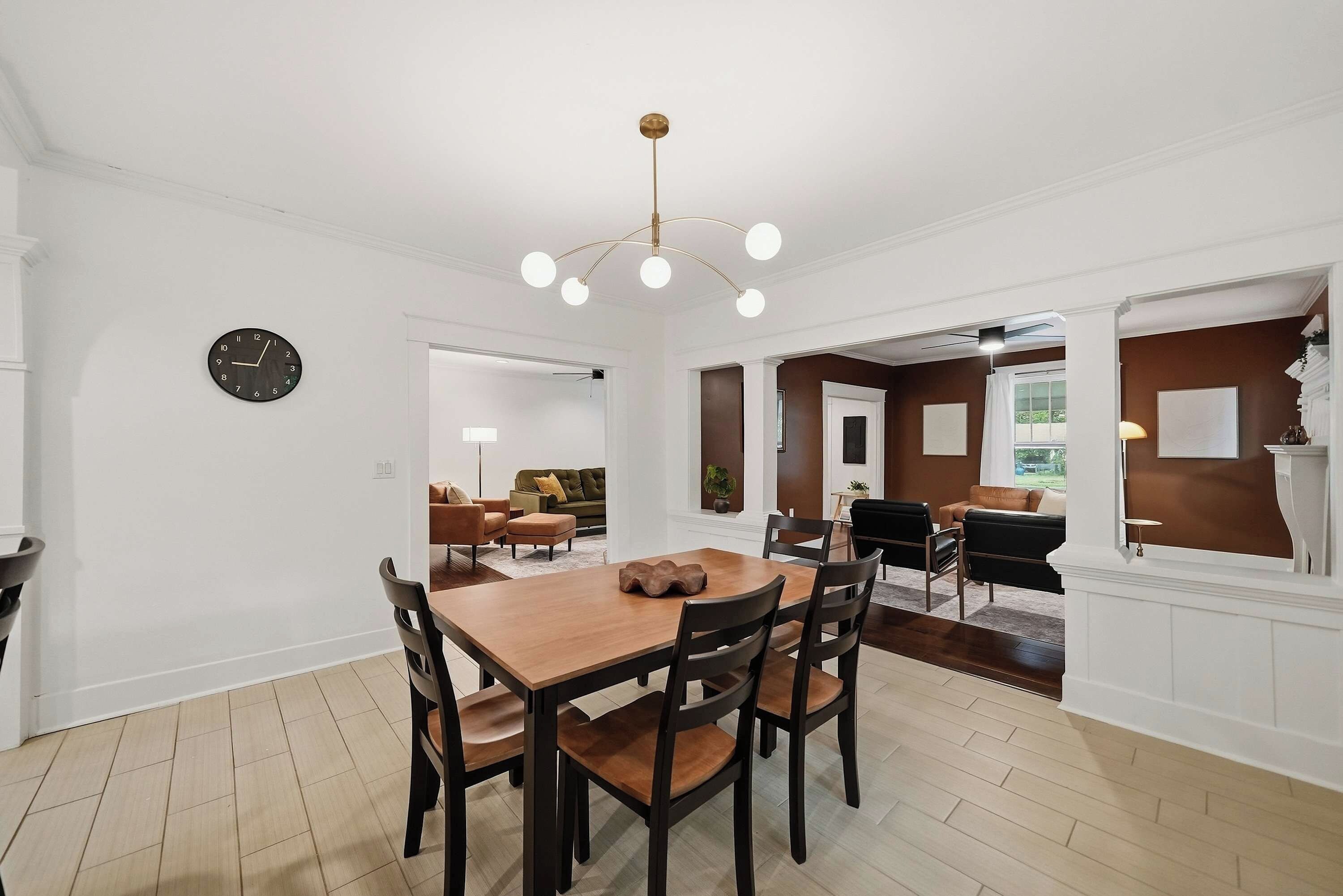 A dining area with a wooden table and chairs, a clock on the wall, and a modern chandelier.