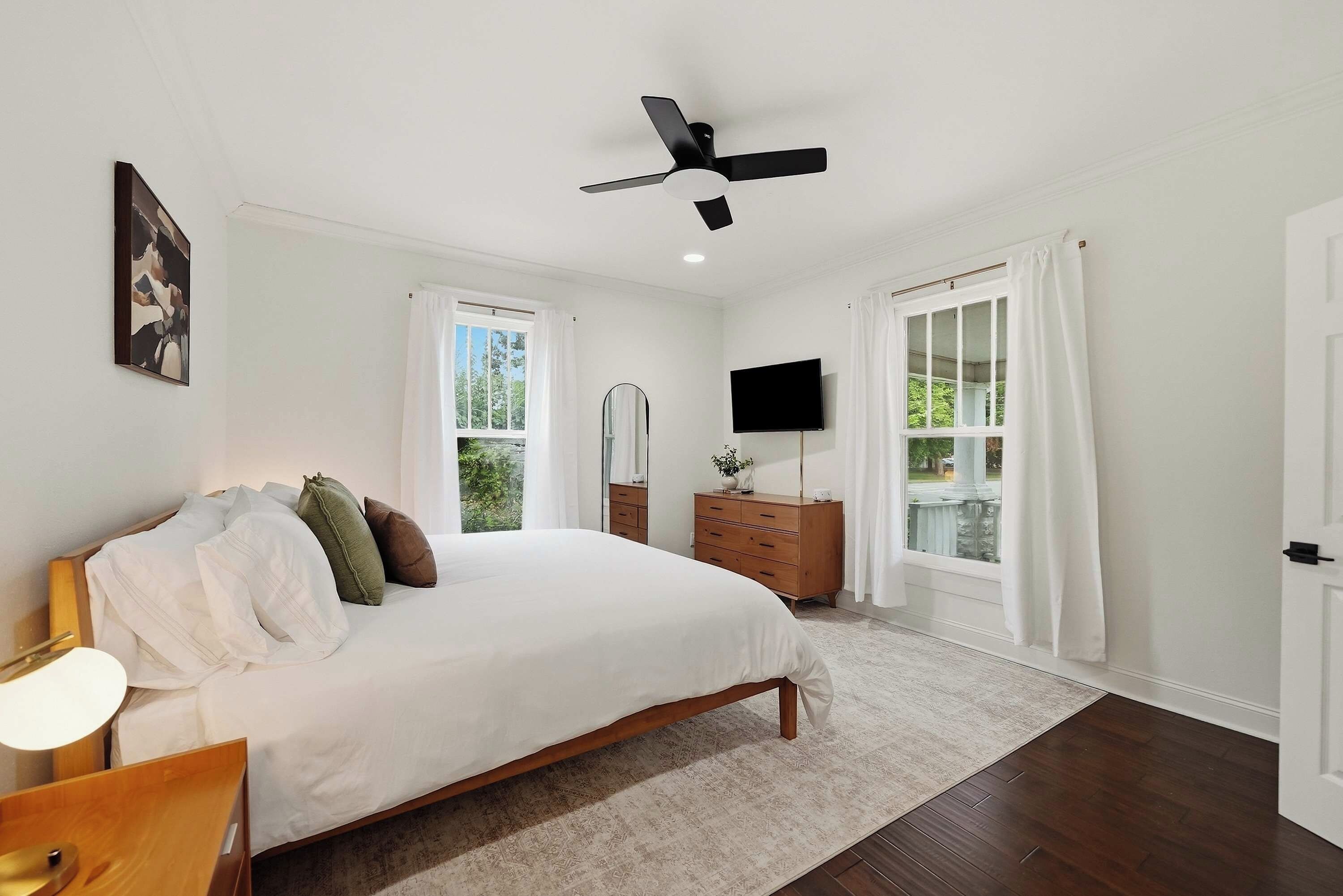A bedroom with a bed, a ceiling fan, a TV, and a window with curtains.