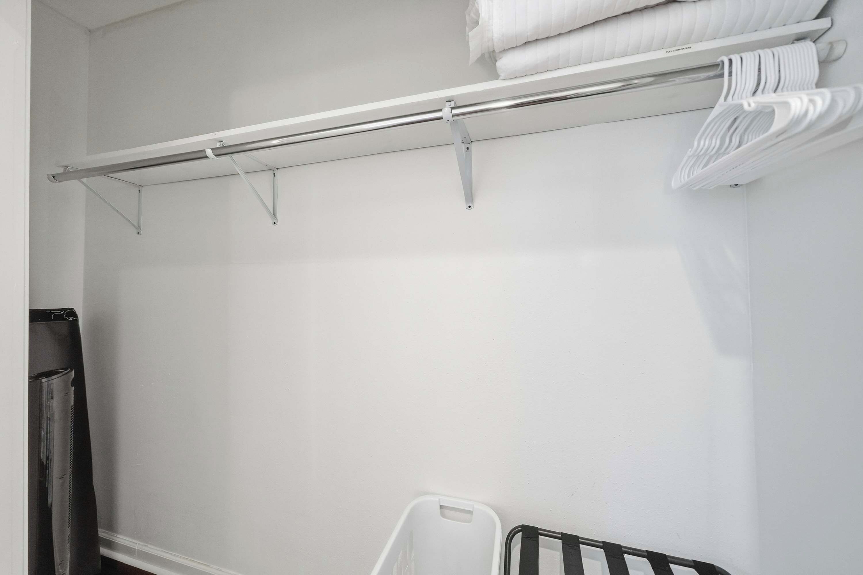 A white closet with a metal rod for hanging clothes and a white plastic basket.