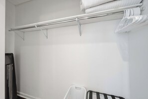 A white closet with a metal rod for hanging clothes and a white plastic basket.