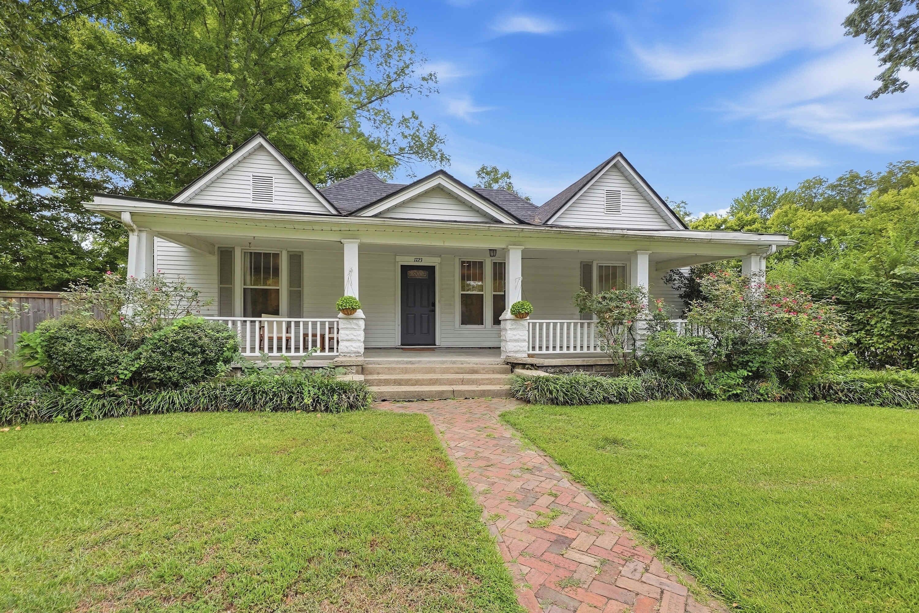 A two-story house with a front porch, a brick pathway leading to the entrance, and a well-maintained lawn.
