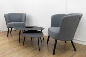 Ein Zimmer mit zwei grauen Sesseln und einem kleinen runden Tisch mit einer Fernbedienung darauf.