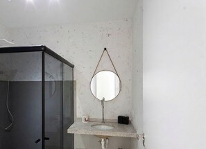 Ein Badezimmer mit Duschkabine aus Glas, einem runden Spiegel an der Wand und einem Waschbecken mit Marmorplatte.