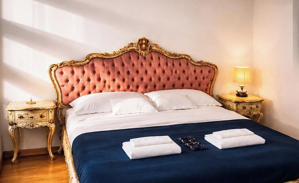 Un lit avec une tête de lit capitonnée, du linge de lit blanc et une couvre-lit bleue. Il y a deux tables de chevet avec des lampes.