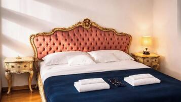 Un lit avec une tête de lit capitonnée, du linge de lit blanc et une couvre-lit bleue. Il y a deux tables de chevet avec des lampes.