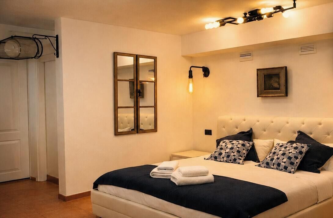 A hotel room with a bed, a nightstand, a wall-mounted light fixture, a mirror, and a framed picture.