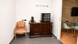 Una habitación con un armario de madera, televisor, un sillón cómodo y una mesa de vidrio con sillas.
