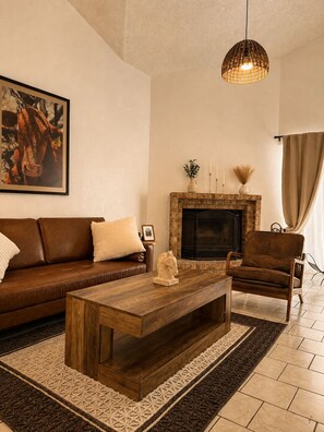 A living room with a brown leather sofa, a wooden coffee table, a fireplace, and a hanging light fixture.