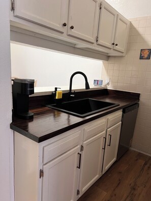 A kitchen with white cabinets, a black countertop, a sink, a coffee maker, and a dishwasher.