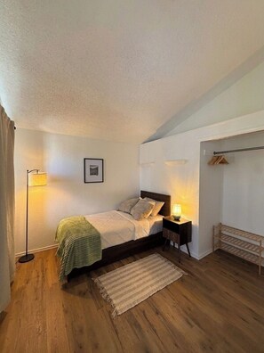 A bedroom with a bed, bedside lamps, a picture on the wall, and a wooden floor.