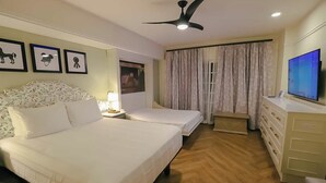 Habitación de hotel con dos camas, ventilador de techo, televisión y ventana con cortinas.
