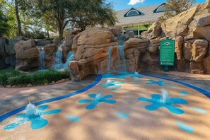 Ein Wasserspiel mit einem Schild, das das Tauchen verbietet, umgeben von großen Felsen und einer gepflasterten Fläche mit blauen Mustern.