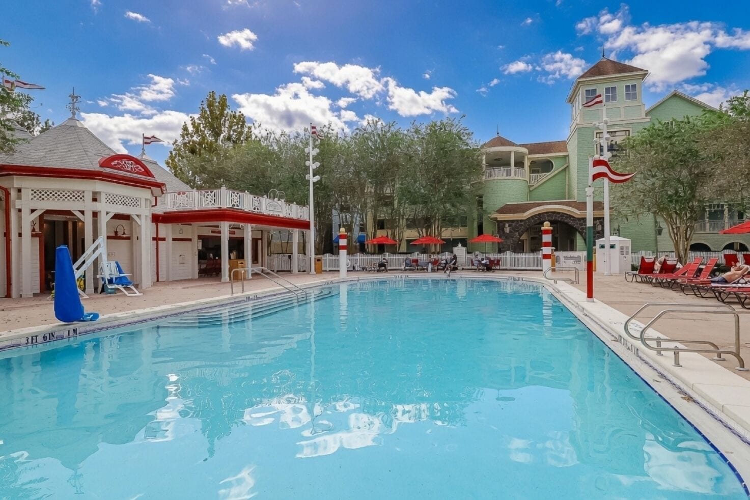 A swimming pool with lounge chairs and umbrellas, surrounded by buildings with a colonial architectural style.