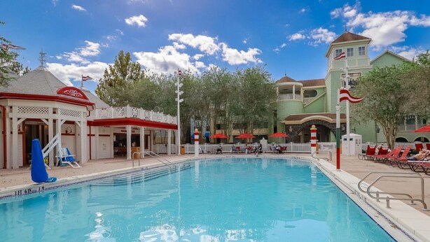 Una piscina con sillas de descanso y sombrillas, rodeada de edificios de estilo colonial.