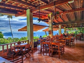 Un restaurant en plein air avec des tables et des chaises en bois, un sol carrelé et une vue sur l’océan.