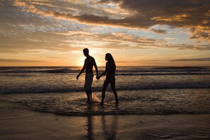 Twee personen wandelen over een strand bij zonsondergang.